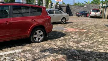 Un estacionamiento pavimentado con varios automóviles, un letrero de hotel y una entrada porticada con detalles decorativos.