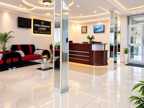 A hotel lobby with a reception desk, a sofa, a coffee table, and a TV screen.