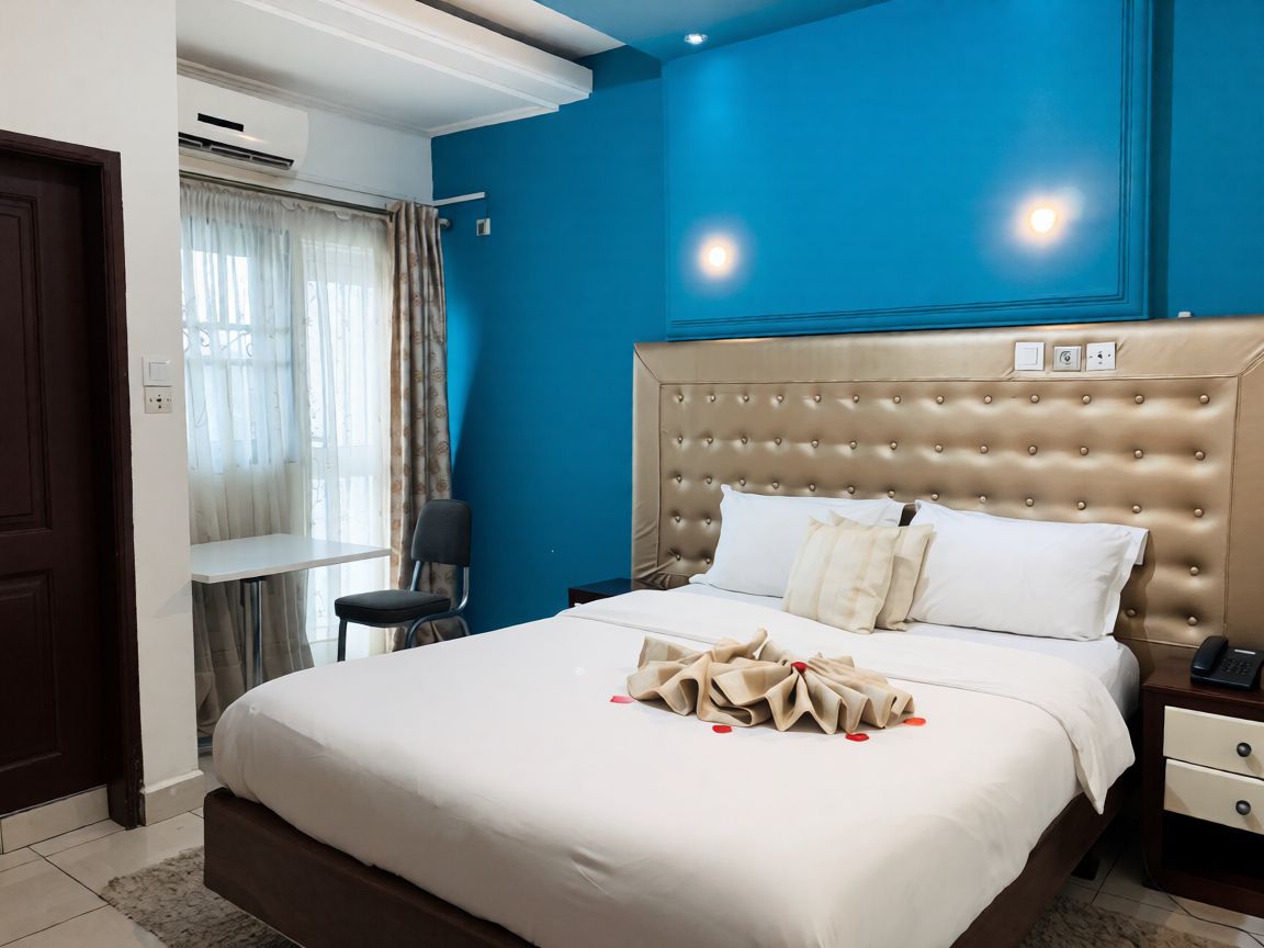 A hotel room with a large bed, a bedside table, a chair, and a window with curtains.