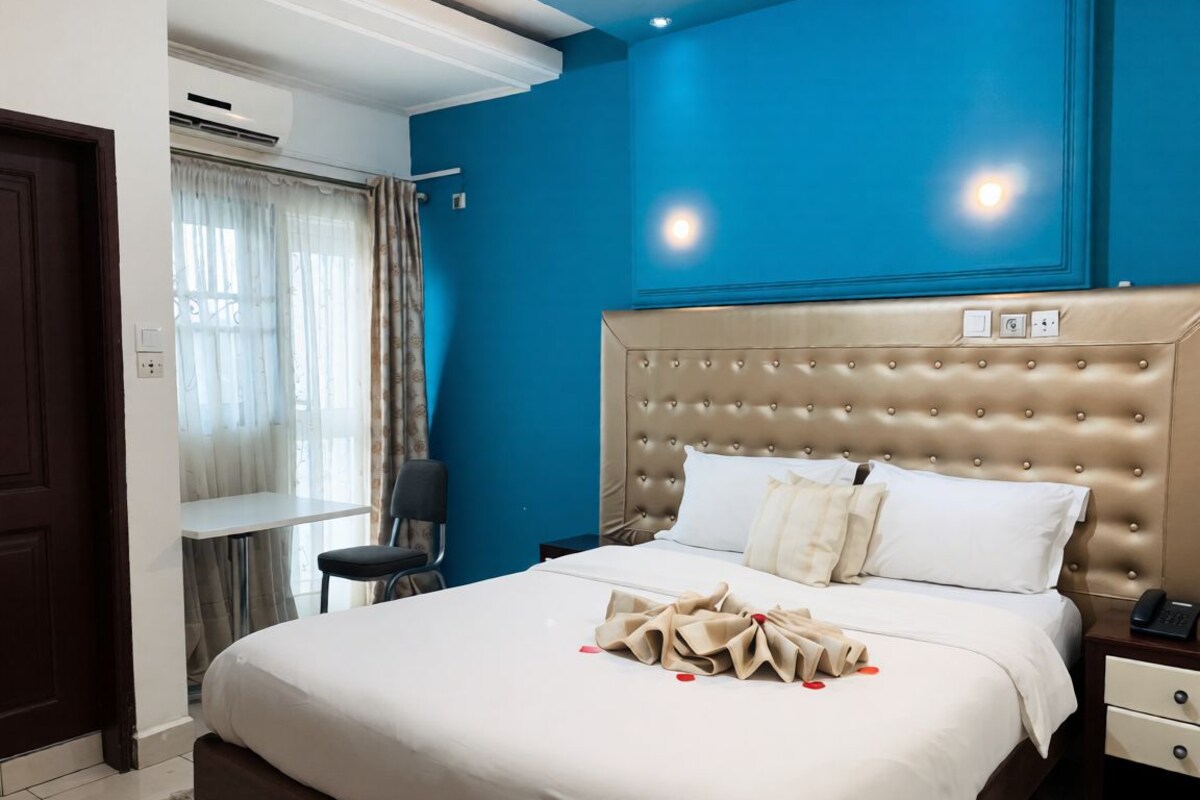 Une chambre d’hôtel avec un grand lit, une table de chevet, une chaise et une fenêtre avec des rideaux.
