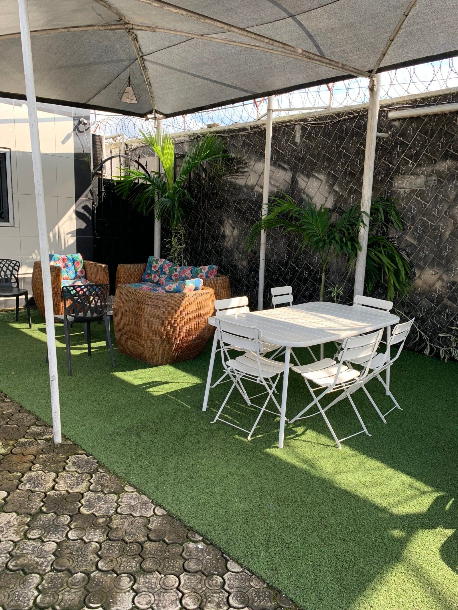 Eine Außenpatio mit Tisch und Stühlen, umgeben von Kunstgrasanlage, einer überdachten Sitzgelegenheit und einem dekorativen Zaun.