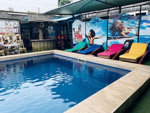 Una piscina con sillas de descanso y un área de bar con asientos junto a la piscina.