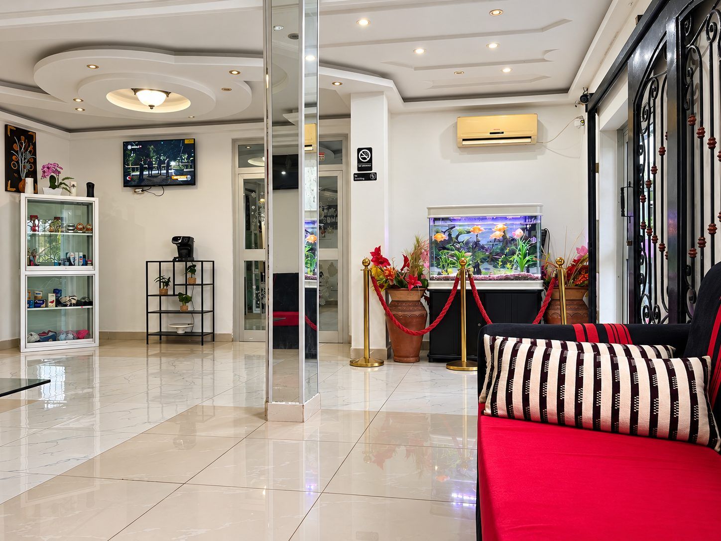 Un vestíbulo de hotel con una mesa de recepción, una pantalla de televisión, un acuario y un sofá rojo.