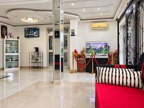 A hotel lobby with a reception desk, a television screen, a fish tank, and a red sofa.