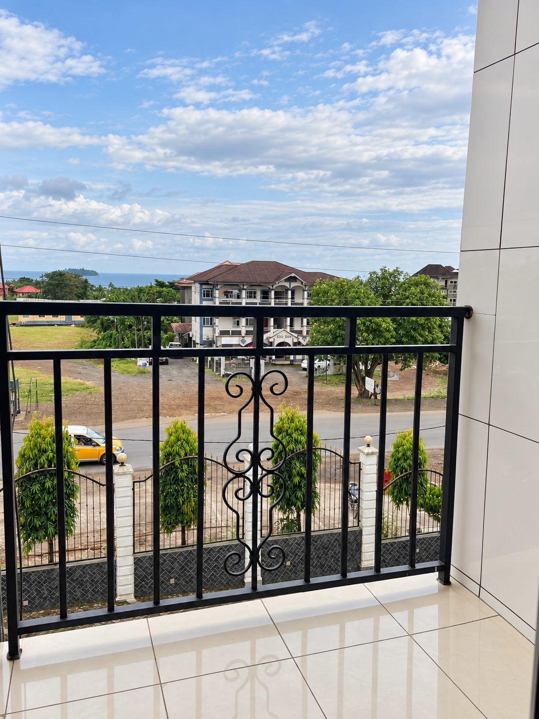 A balcony with a view of a street, a building, and a clear sky.