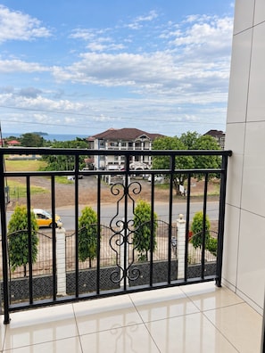 A balcony with a view of a street, a building, and a clear sky.
