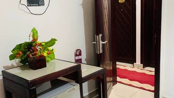 A room with a television mounted on the wall, a table with a plant, a refrigerator, and a door with a number plate.