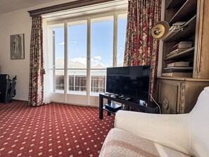 A hotel room with a large window, a flat-screen TV, a bookshelf, and a red patterned carpet. - Fullun 14 by Interhome (St. Moritz)