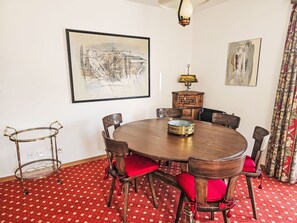 A dining room with a round wooden table, six chairs with red cushions, a chandelier, and two framed artworks on the walls. - Fullun 14 by Interhome (St. Moritz)