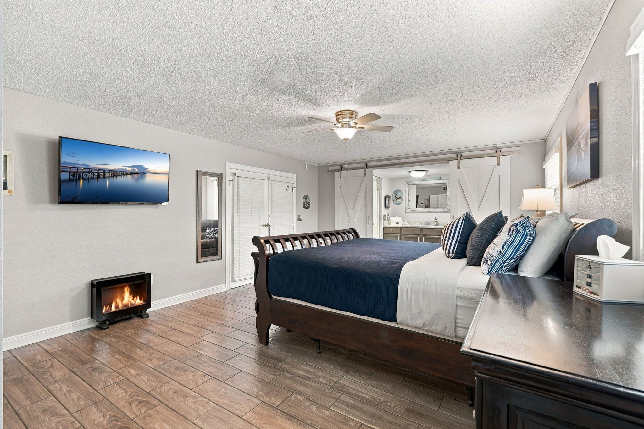 A bedroom with a bed, a TV, a fireplace, and a ceiling fan.
