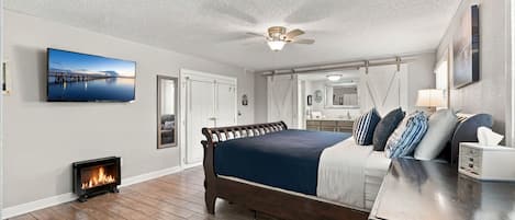 A bedroom with a bed, a TV, a fireplace, and a ceiling fan.