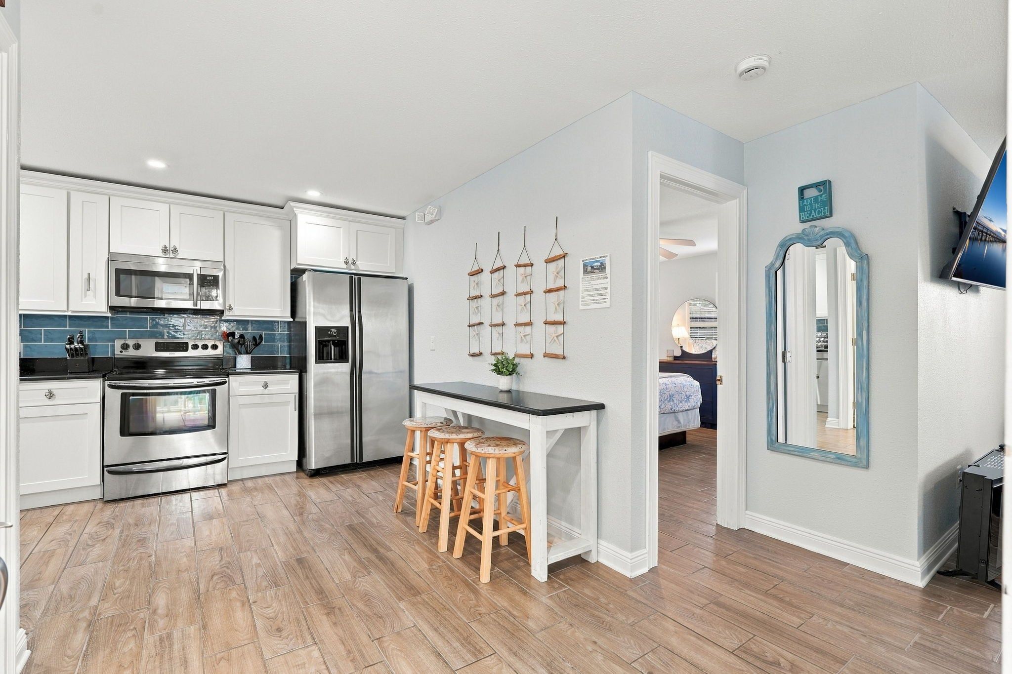 A modern kitchen with stainless steel appliances, a wooden bar stool seating area, and a view into a bedroom.