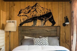 Ein Bett mit Kopfteil, einer Wandlampe und einer dekorativen Bergsilhouette.