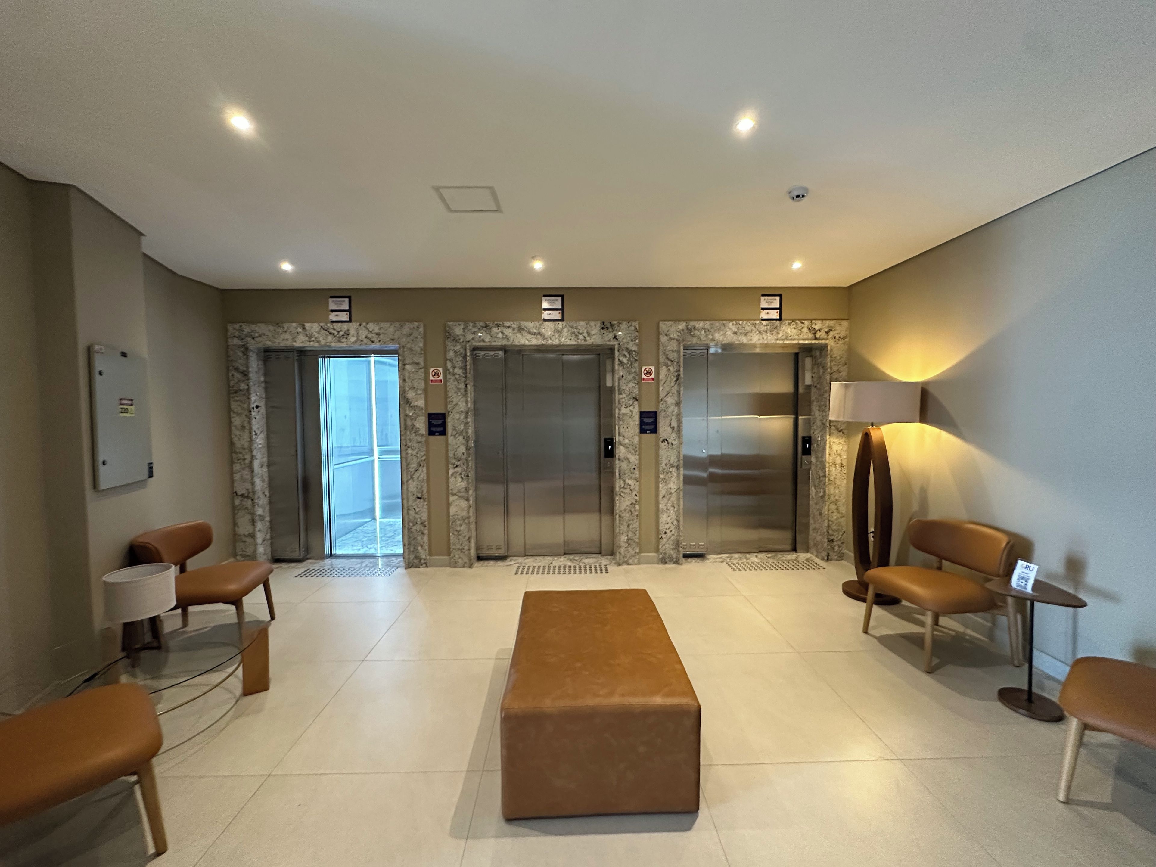 A lobby with marble walls, two elevators, seating area, and a reception desk.