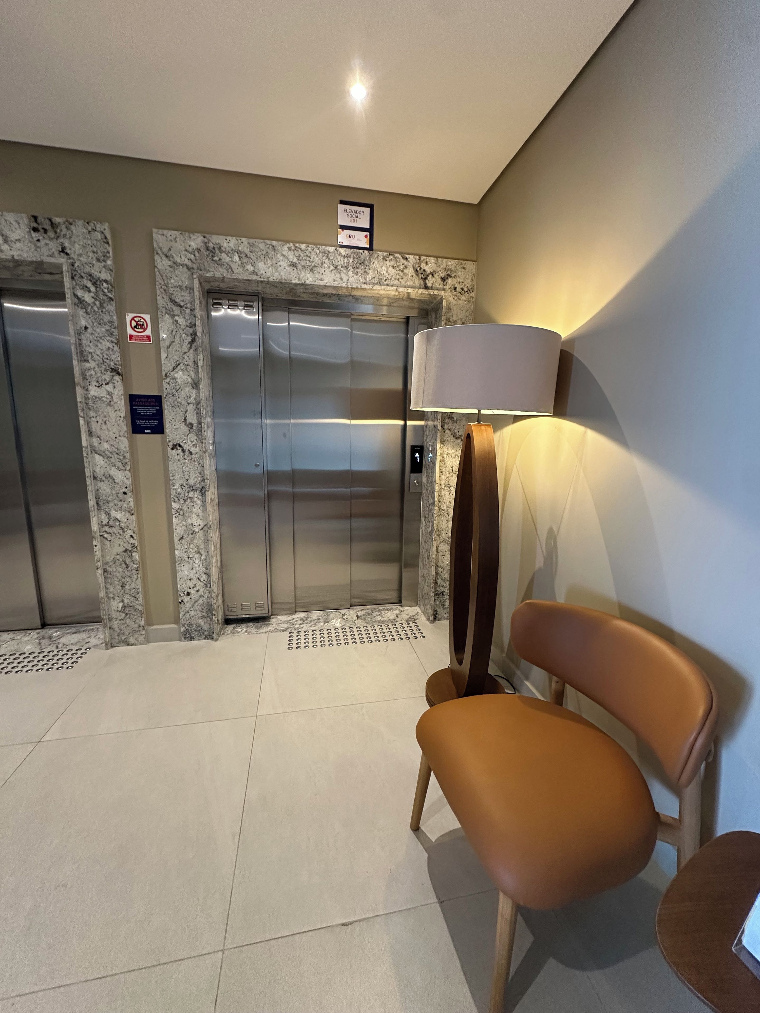 An elevator area with marble walls, a chair, and a lamp.