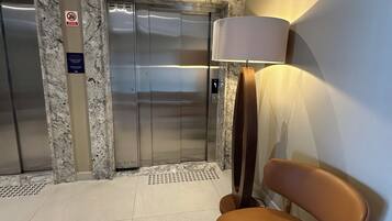 An elevator area with marble walls, a chair, and a lamp.