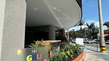 A modern building entrance with a sign for '181 GRU RESIDENCE' and a landscaped area with plants.