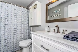 A bathroom with a white toilet, a sink with a mirror above it, and a shower curtain with a zigzag pattern. - Always 5 O'clock - Lagoon Front, Private Beach Access, Pool & Kayaks (Gulf Shores)