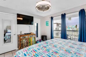 A bedroom with a bed, a television, a dresser, and a balcony with curtains. - Always 5 O'clock - Lagoon Front, Private Beach Access, Pool & Kayaks (Gulf Shores)