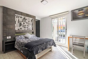 A modern bedroom with a bed, a large abstract wall art piece, a window with a view of the outside, and a chair.