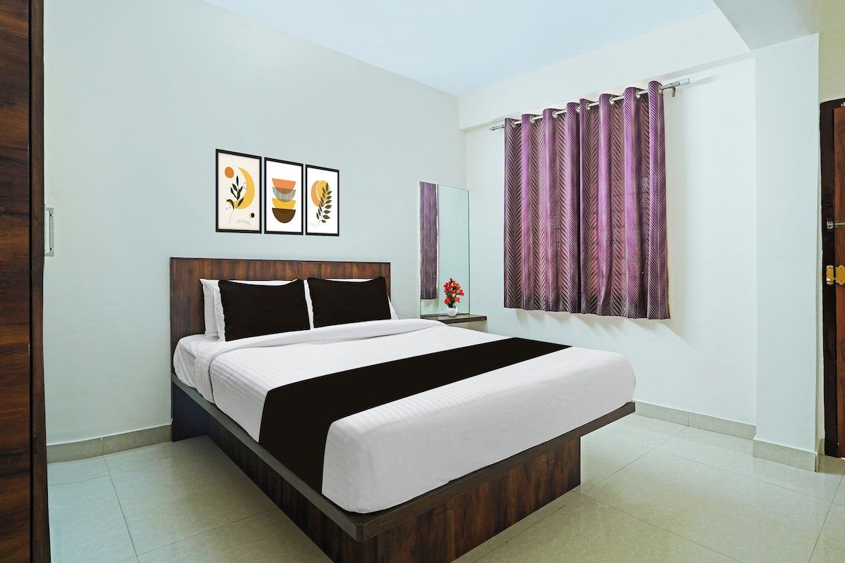 A bedroom with a bed, a nightstand, a mirror, and a window with curtains.