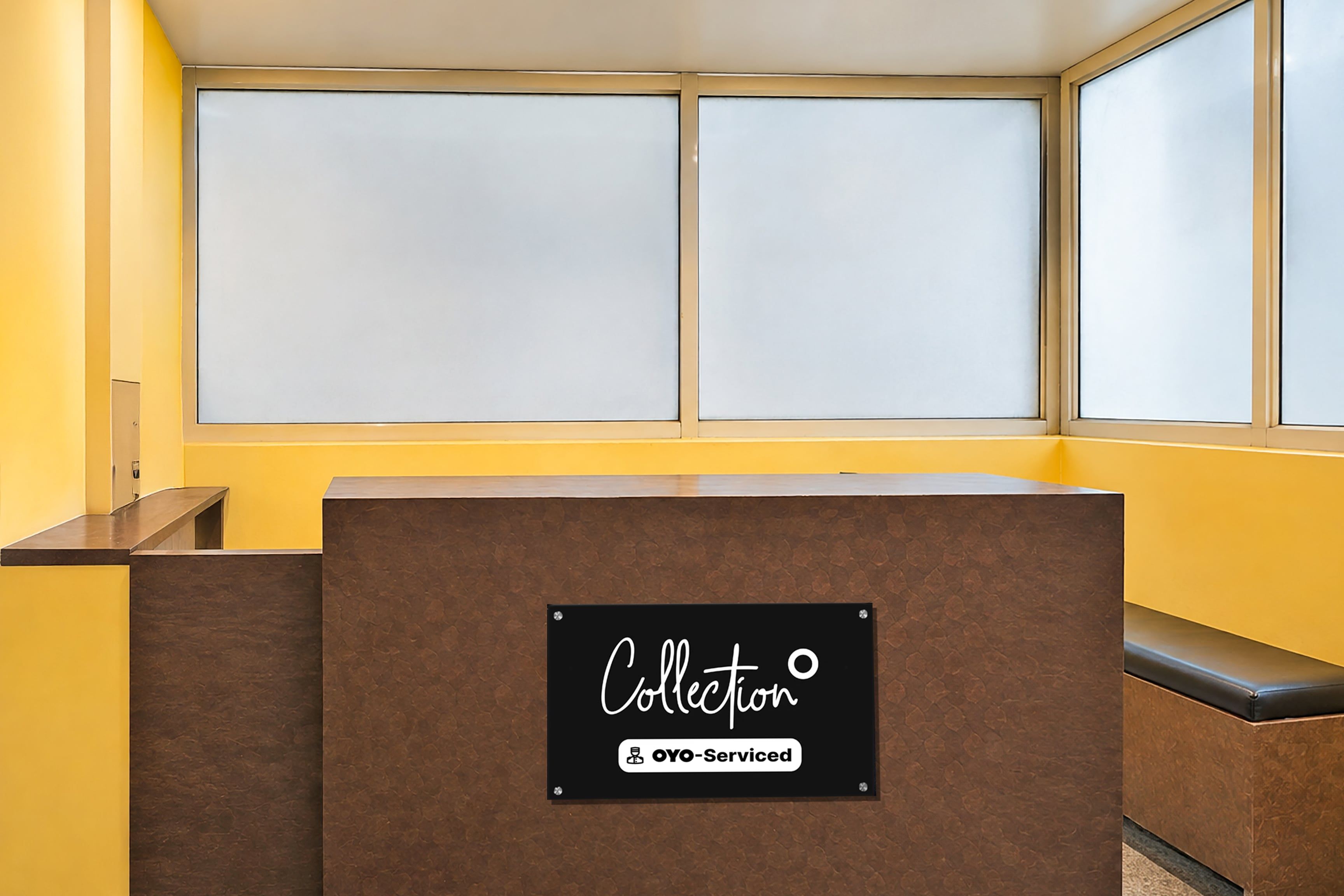 Un comptoir d’accueil avec une pancarte indiquant « Collecte » et « Service OYO », situé dans une pièce aux murs jaunes et aux grandes fenêtres.