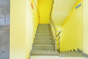 A staircase with a metal railing, a fire exit sign, and a street sign on the wall. - Collection O Virajpete Bus Terminal (Coorg)