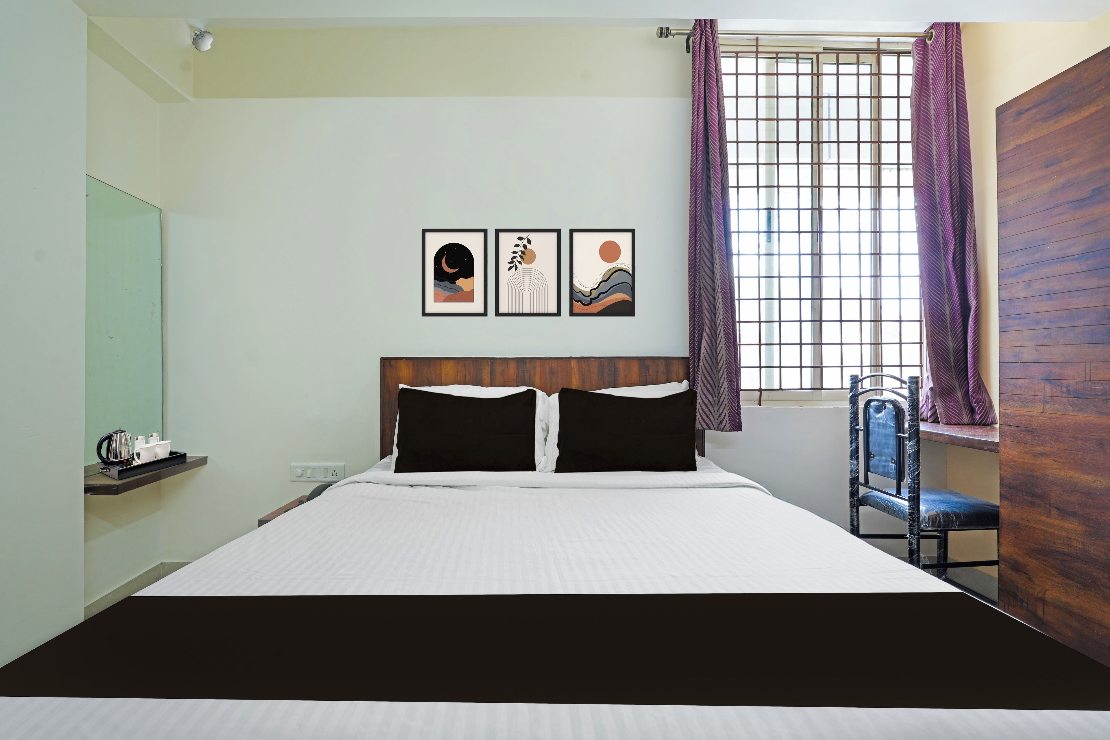Una habitación de hotel con una cama, un ventanal con cortinas, una silla y tres cuadros en la pared.
