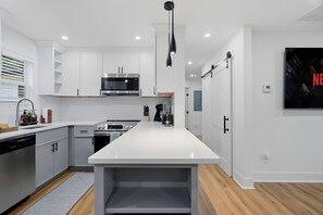 Une cuisine moderne avec des meubles blancs, un îlot central, des appareils en acier inoxydable et un luminaire suspendu.