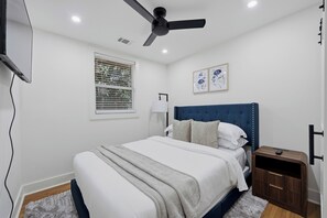 Une chambre à coucher avec un lit, un ventilateur de plafond, une fenêtre avec des stores et une table de chevet.