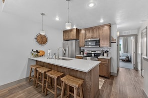 A modern kitchen with wooden cabinets, a central island with stools, stainless steel appliances, and pendant lighting. - The Payette Perch- Pets ok- sleeps 6 (McCall)
