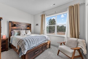 A bedroom with a wooden bed, a nightstand, a chair, a window with curtains, and a wall with a welcome sign. - The Payette Perch- Pets ok- sleeps 6 (McCall)