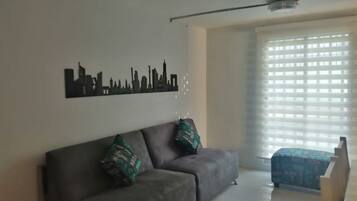 Un salón con un sofá, una obra de arte con un paisaje urbano en la pared y una ventana con persianas.