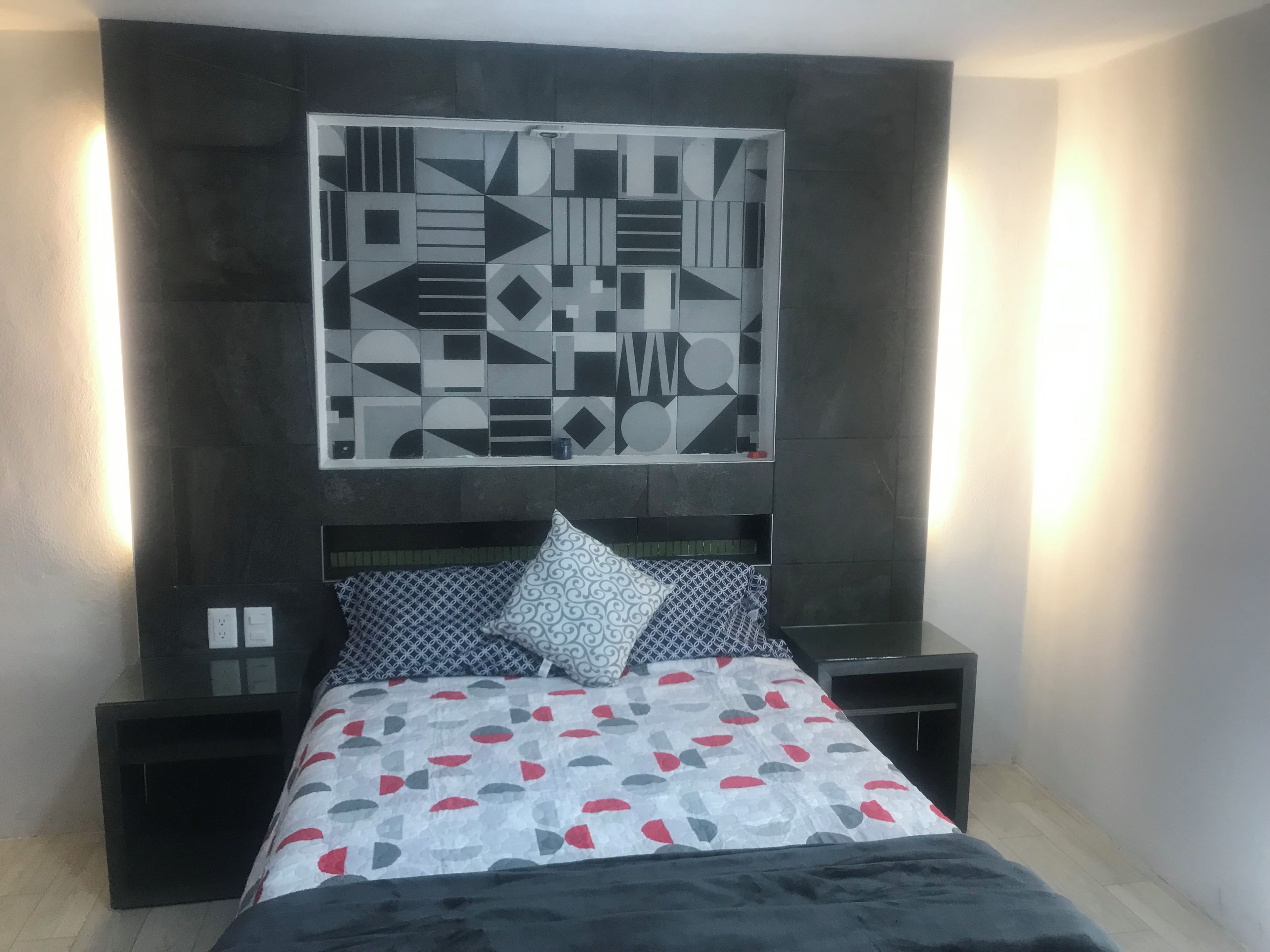 Un dormitorio con cama, mesita de noche, una obra de arte en la pared y una mesita auxiliar.