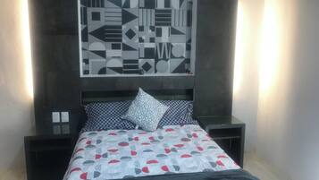 Un dormitorio con cama, mesita de noche, una obra de arte en la pared y una mesita auxiliar.
