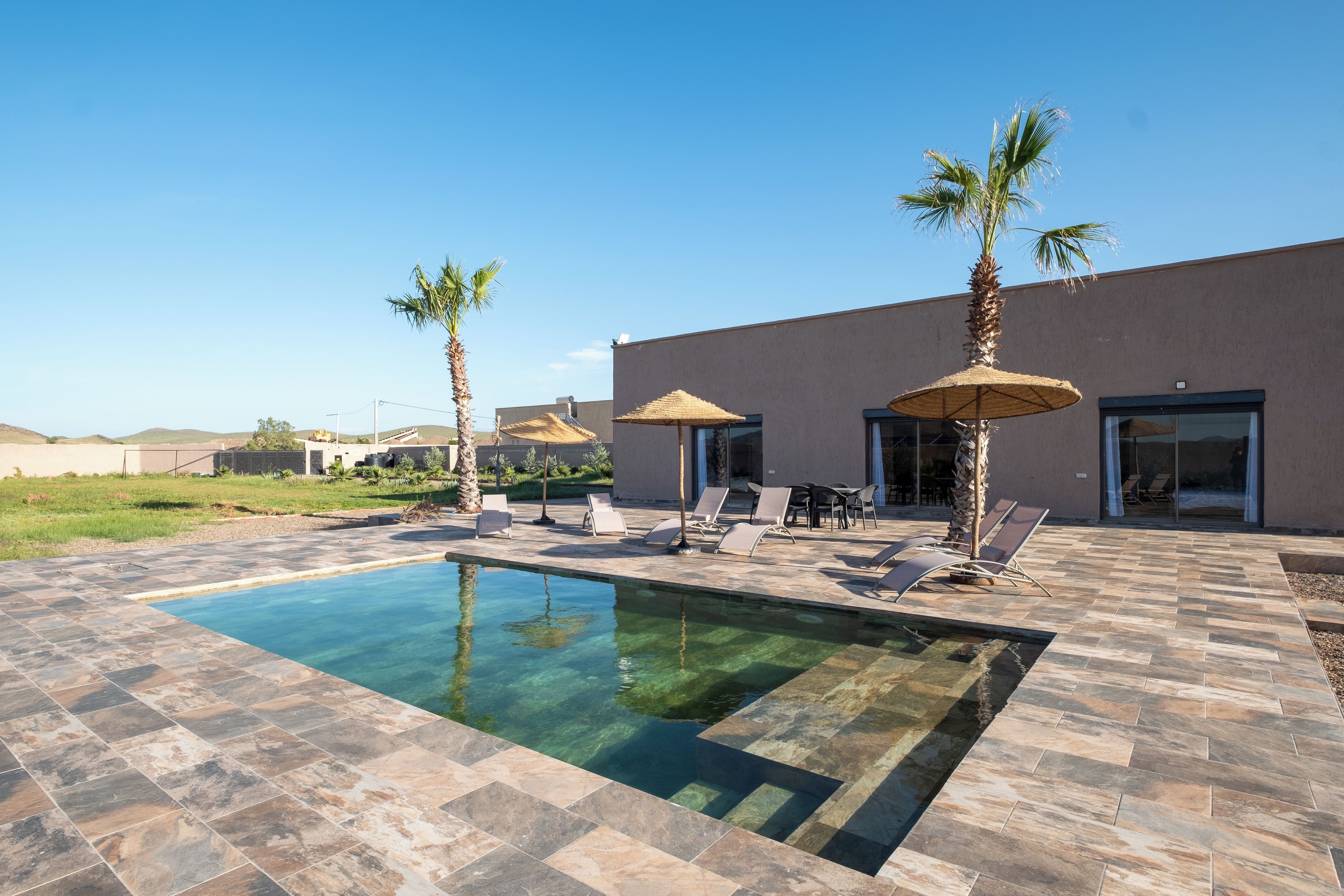 A swimming pool with lounge chairs and umbrellas, surrounded by a modern building with a flat roof.