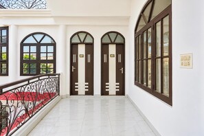 Un pasillo con dos puertas, una escalera con alfombra roja y una ventana con barandilla de metal.