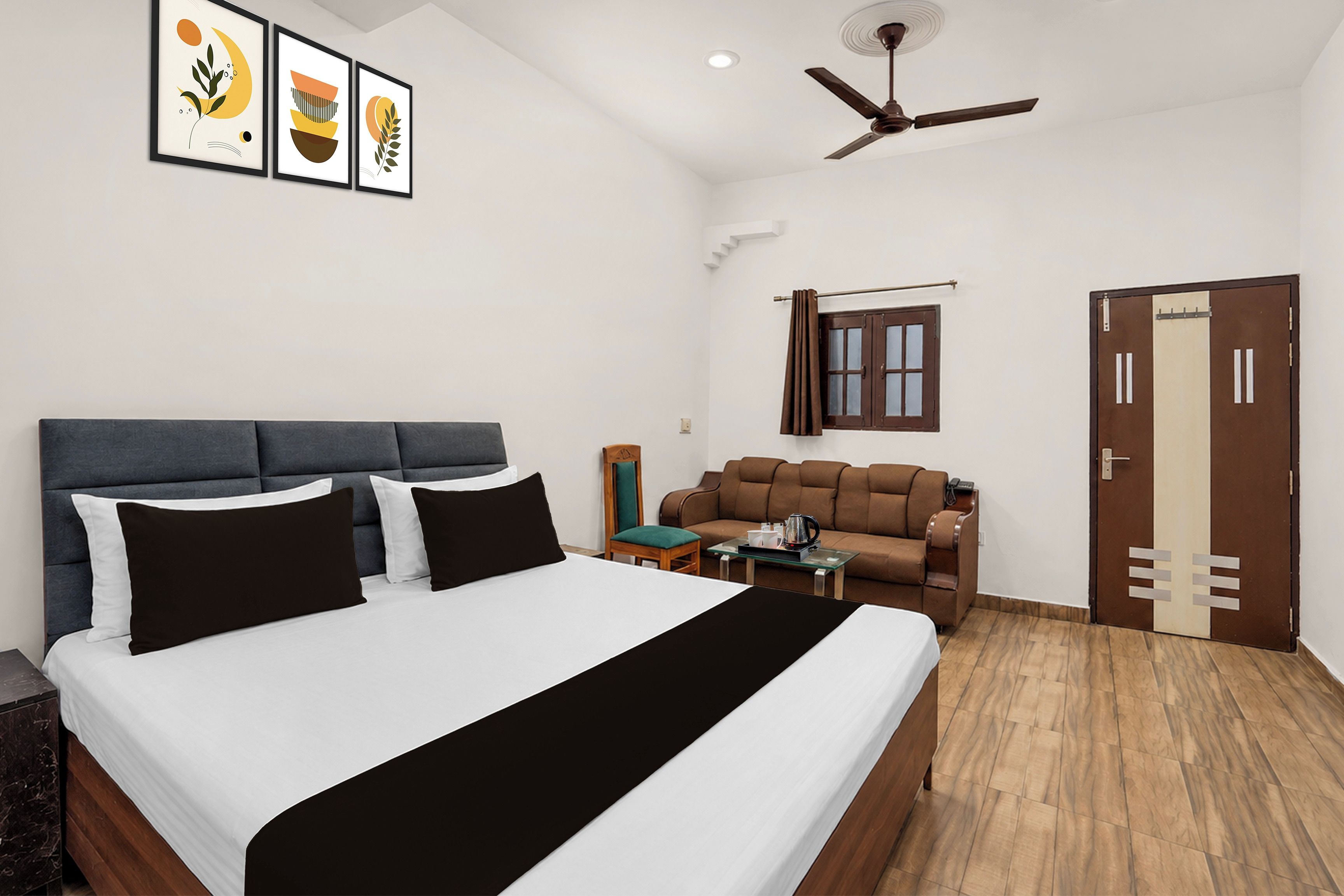 A hotel room with a bed, a sofa, a coffee table, a ceiling fan, and a door.