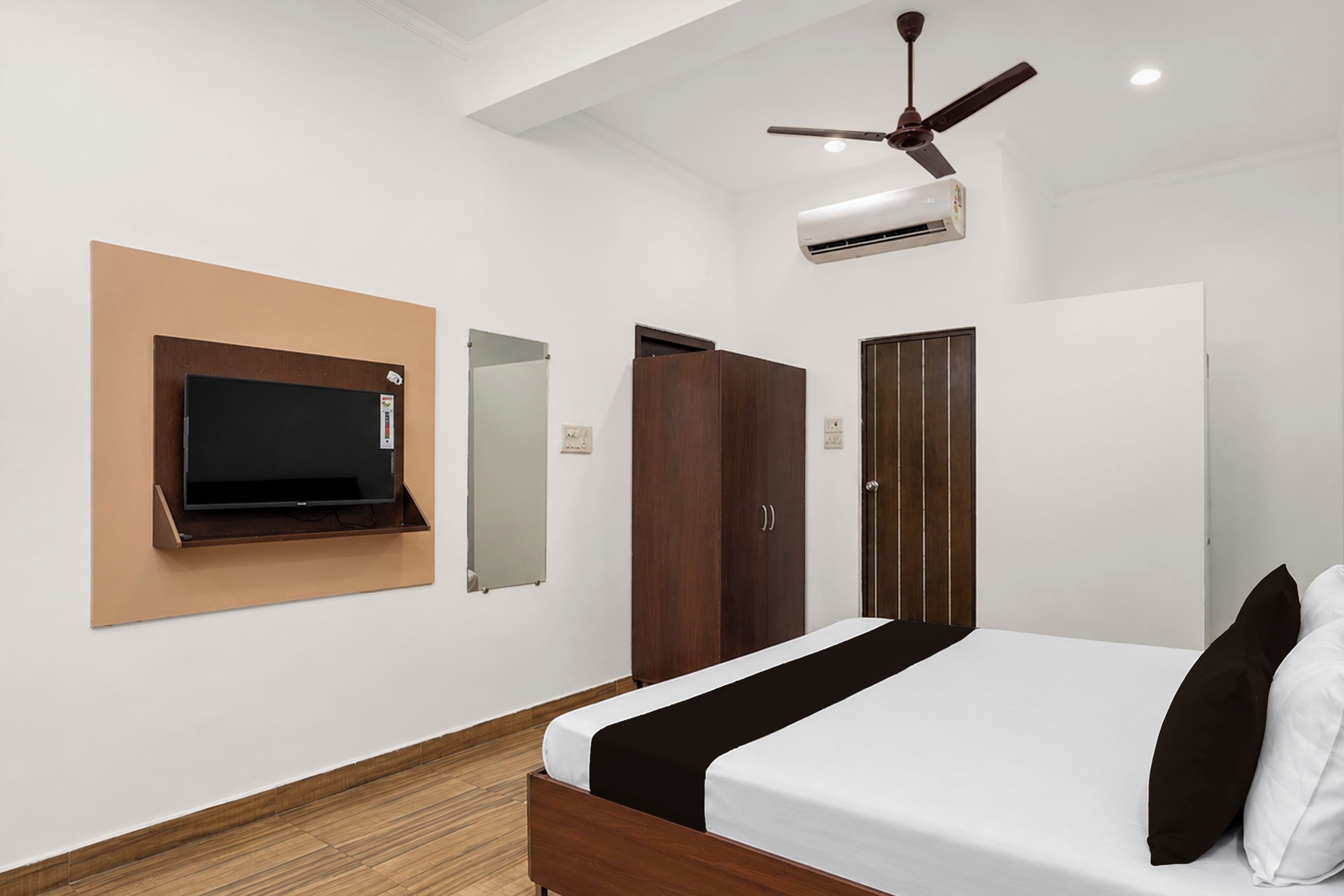 A bedroom with a bed, a TV mounted on the wall, a wardrobe, and a ceiling fan.