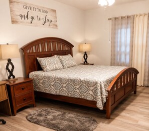 Un dormitorio con una cama de madera, dos mesitas de noche, una alfombra y una pared con una frase inspiradora.