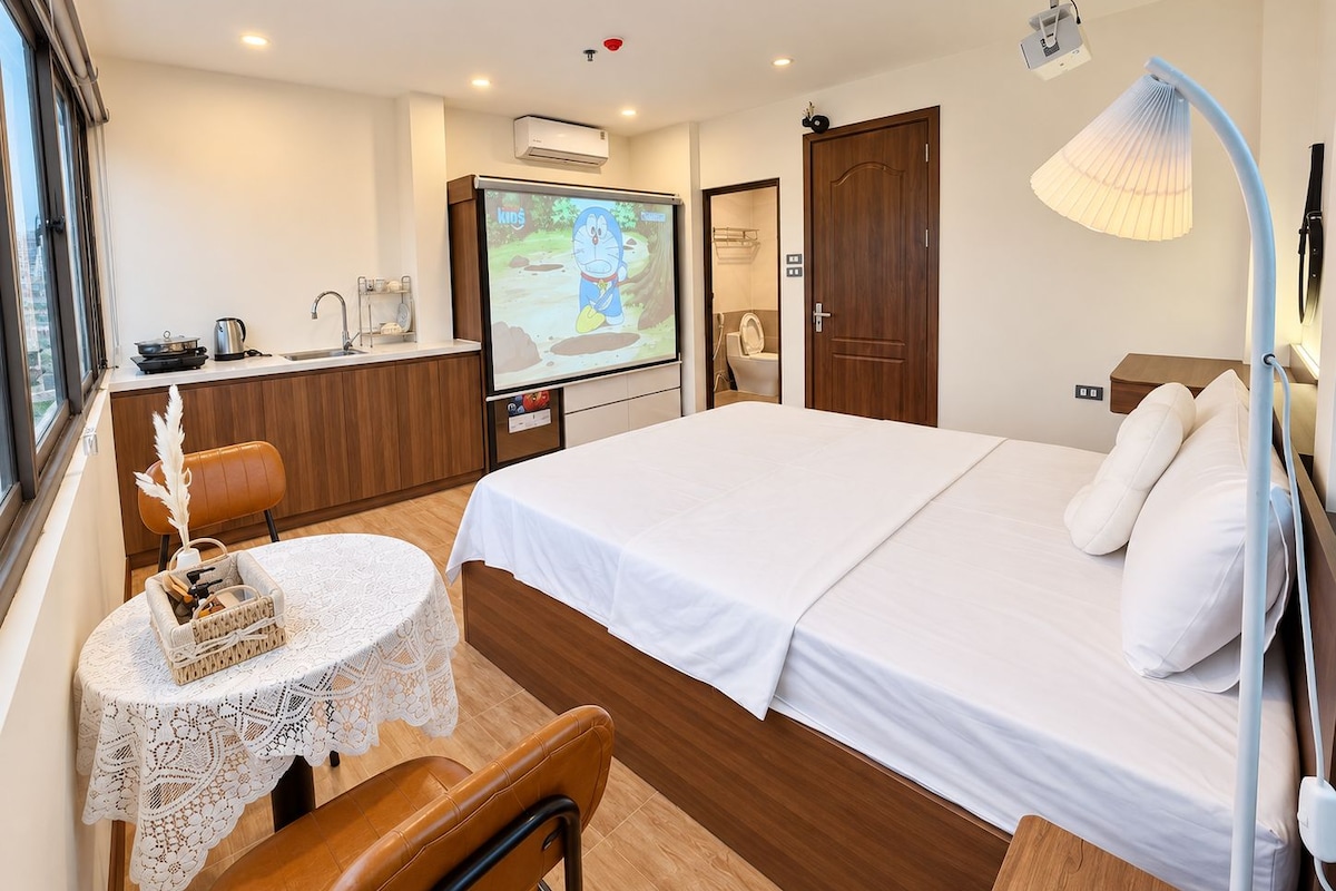 Una habitación de hotel con una cama, un escritorio con una computadora portátil, una silla, una mesa con una cesta, un televisor y la puerta del baño.