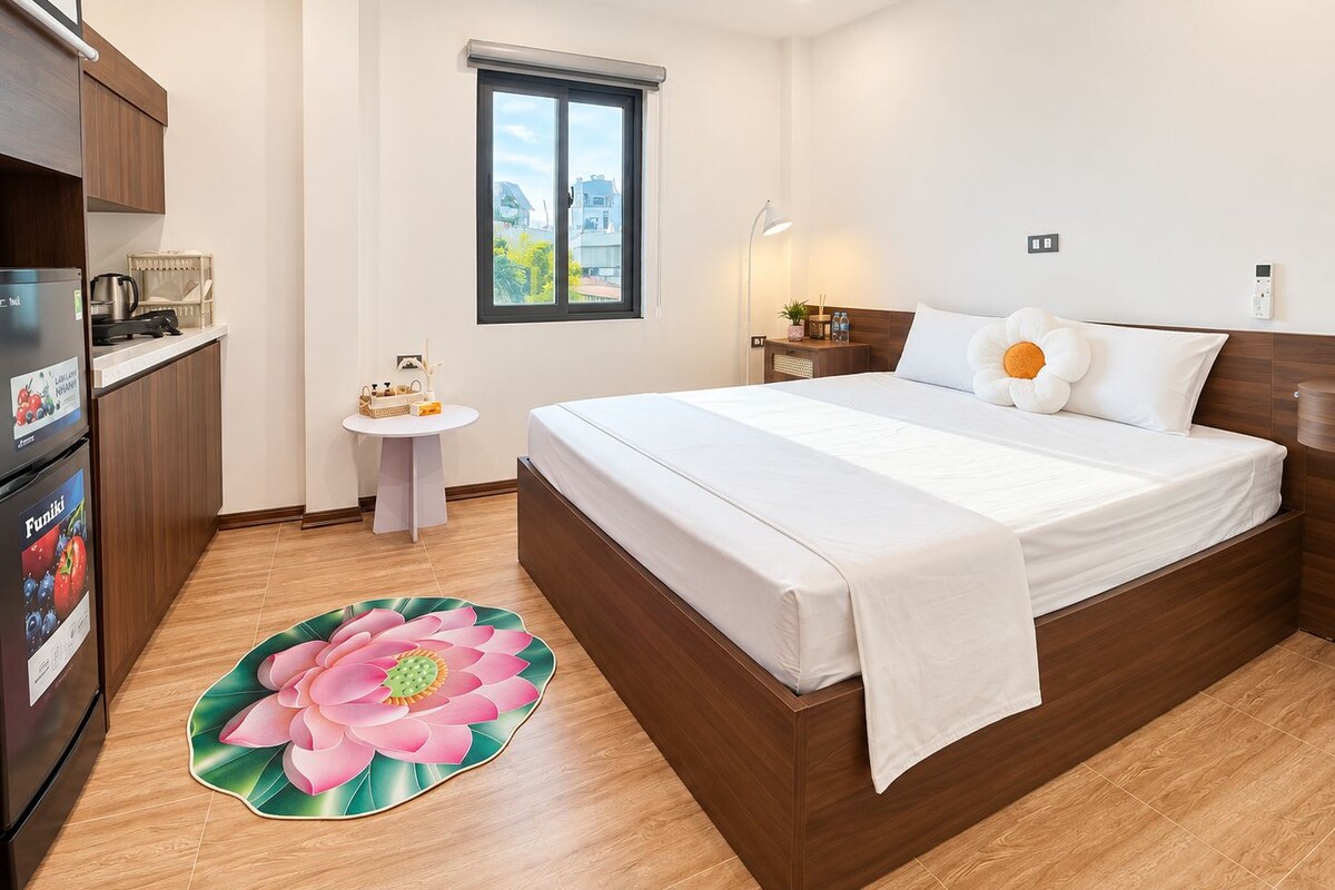 Habitación de hotel con cama, una mesita, refrigerador, ventana y baño.