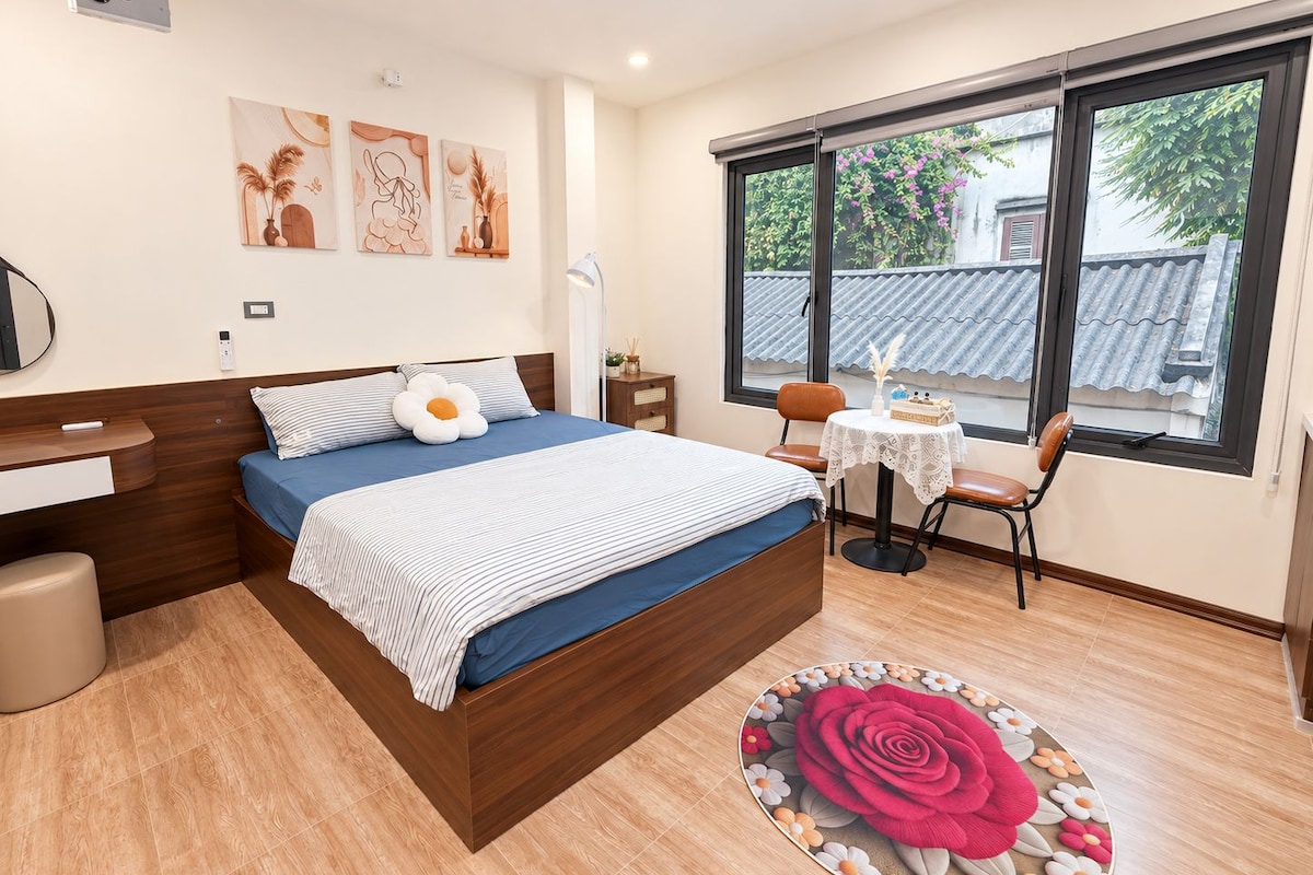 Un dormitorio con cama, mesita de noche, silla y ventana con vistas al exterior.