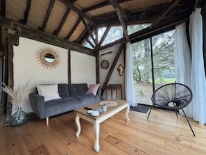 A room with a wooden ceiling, a gray sofa, a wooden coffee table, a black chair, and a view of the outdoors. - Les Pins Vacation Rental - CAME - Vacation Rental (CAME)