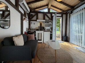 A cozy living area with a sofa, a small table, and a kitchen with a view to the outdoors. - Les Châtaigniers Vacation Rental - CAME (CAME)