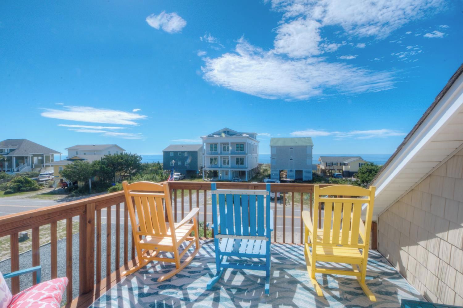 A balcony with three rocking chairs, a patterned floor, and a view of houses and the ocean.