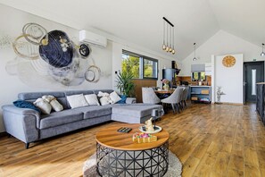 Un salon moderne avec un canapé d’angle gris, une table basse ronde et un grand tableau abstrait accroché au mur.