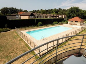 Ein Schwimmbad mit eingezäuntem Deck, umgeben von einer Rasenfläche und einer Reihe von Häusern im Hintergrund.