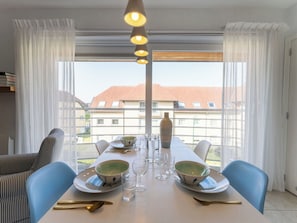 Ein Essbereich mit einem Tisch für zwei Personen, Blick auf Gebäude durch große Fenster und einer hängenden Leuchte.