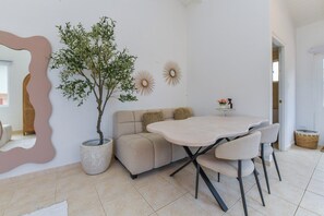 Un espace repas comprenant une table, des chaises, un canapé, un arbre en pot et des éléments de décoration murale.